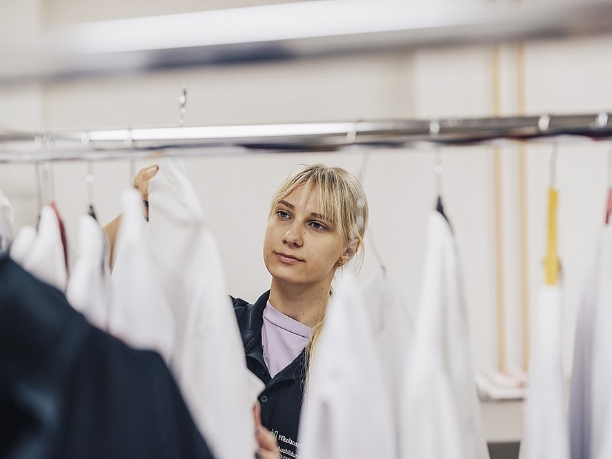 Eine junge Frau steht vor einem Garderobenständer und hängt Kleidung mit Kleiderbügel an die Stange